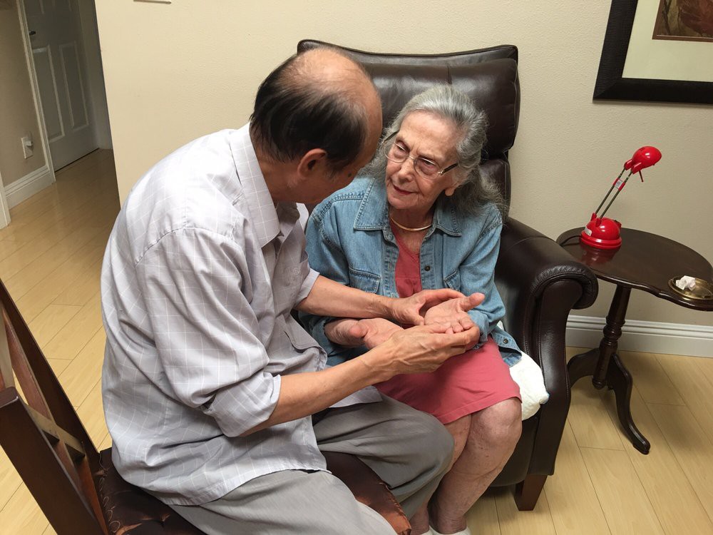 An elderly couple engaged in a heartfelt conversation while holding hands indoors.