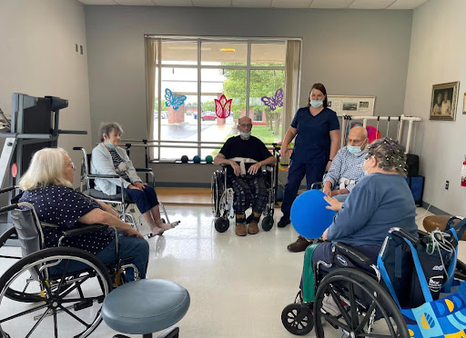 A group therapy session for elderly individuals in wheelchairs, guided by a healthcare professional.