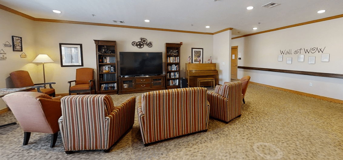 A cozy living room with striped chairs facing a large television, flanked by bookshelves and a piano.