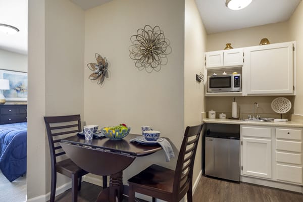 A cozy dining area with a small table and chairs adjacent to a compact kitchen featuring a microwave and fridge.