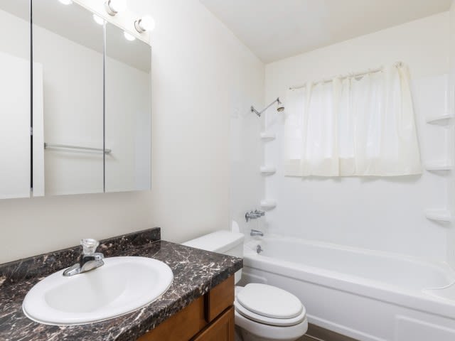 A clean and simple bathroom with a granite countertop, bathtub, and white walls.