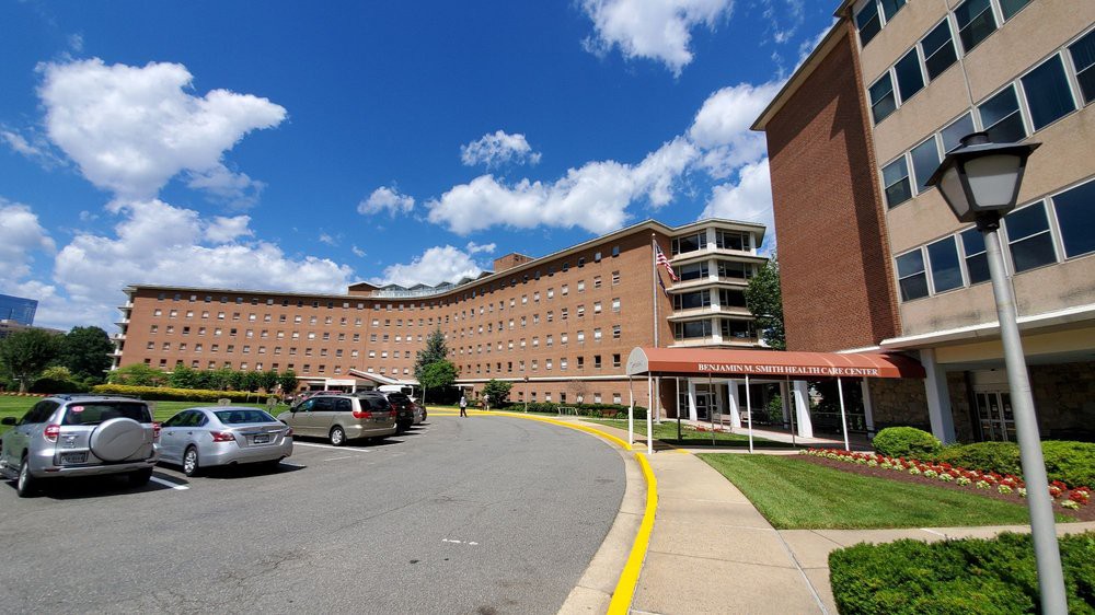 A brick building with a curved design, parking area, and a clear blue sky with clouds.