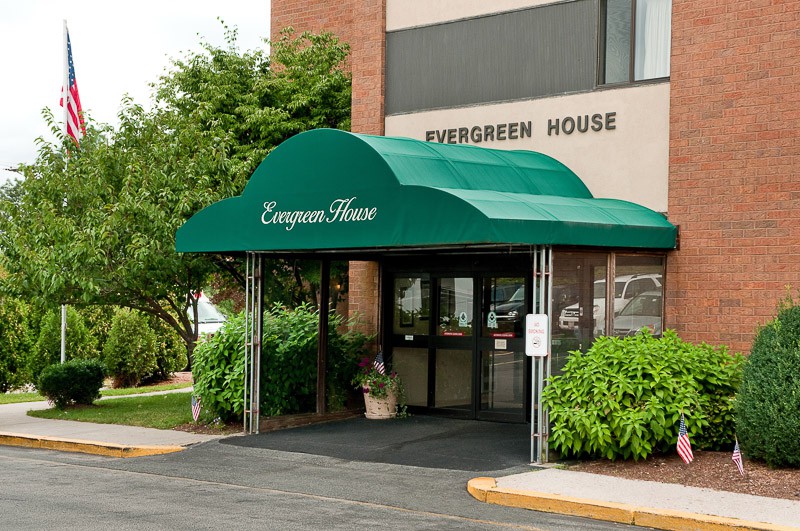 The entrance to Evergreen House, featuring a green awning surrounded by trees and bushes.