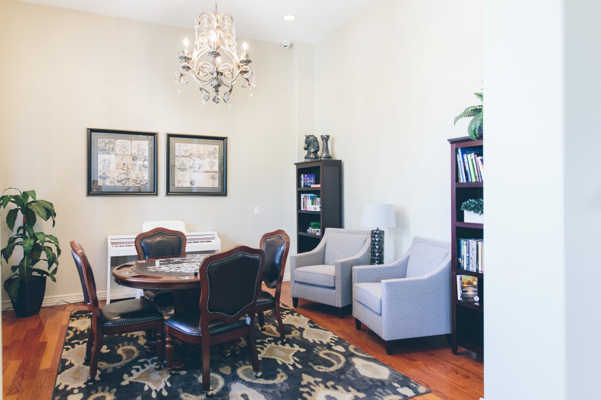 A cozy and elegant living room with classic furniture, featuring a central round table, upholstered chairs, two armchairs, bookcases, and a decorative chandelier.