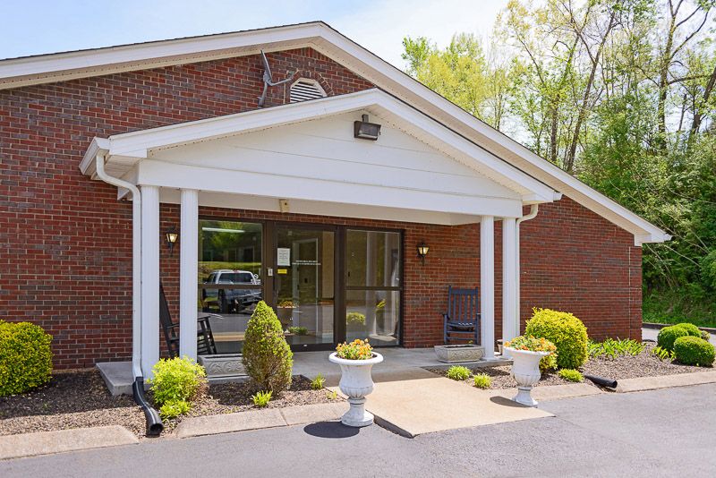 A brick building with a white-columned entrance and landscaped plants.