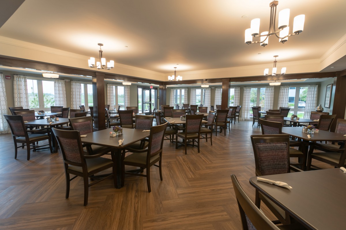 An empty dining room with wooden tables and chairs, featuring elegant lighting fixtures and wood flooring.