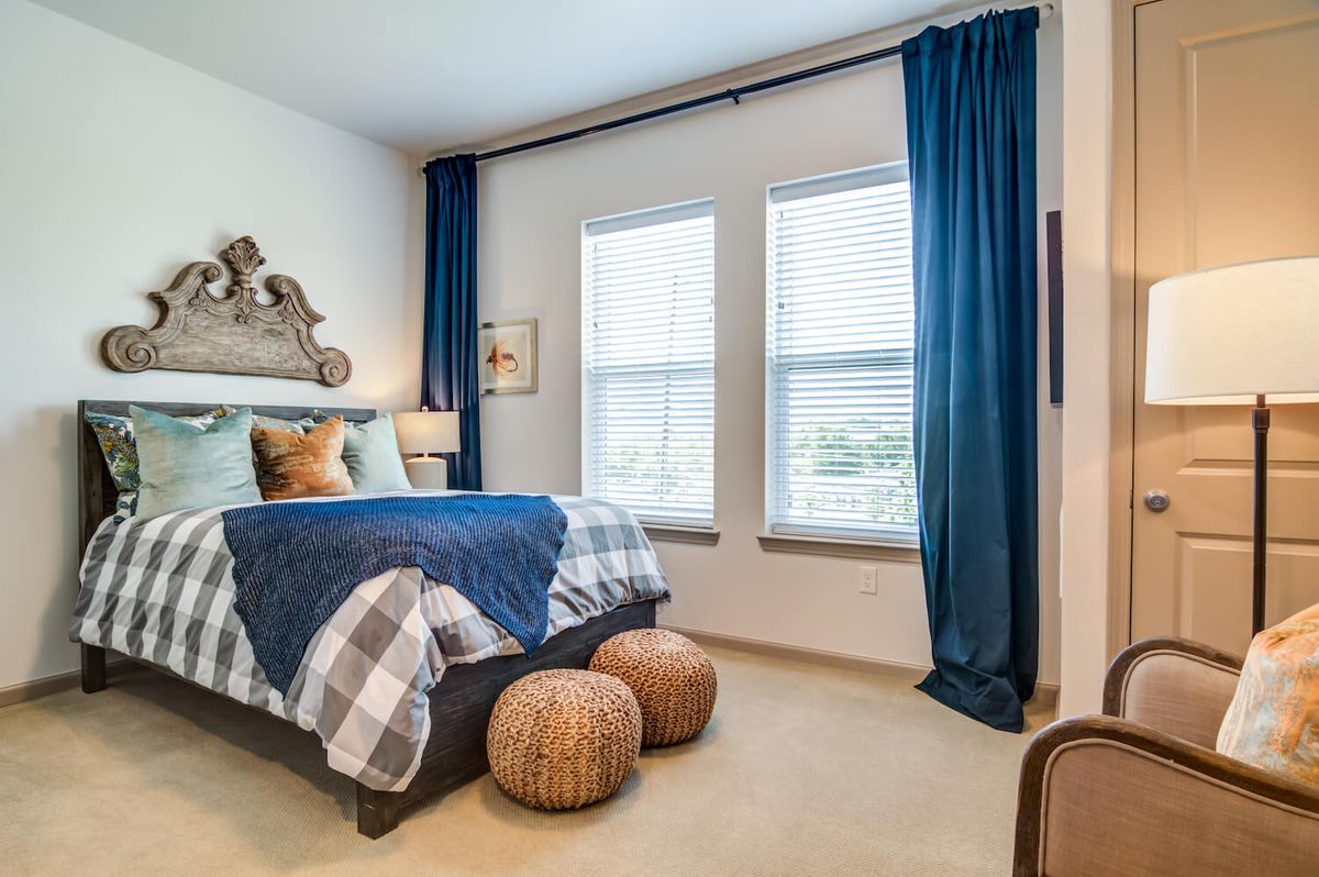 A cozy bedroom featuring a neatly made bed with blue accents, large windows with blue curtains, and decorative elements creating a serene atmosphere.