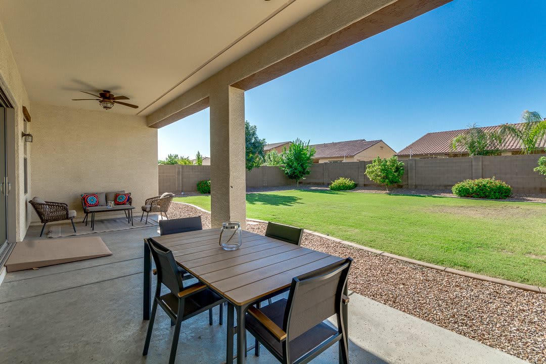 A cozy patio with a dining set, overlooking a spacious backyard lawn.