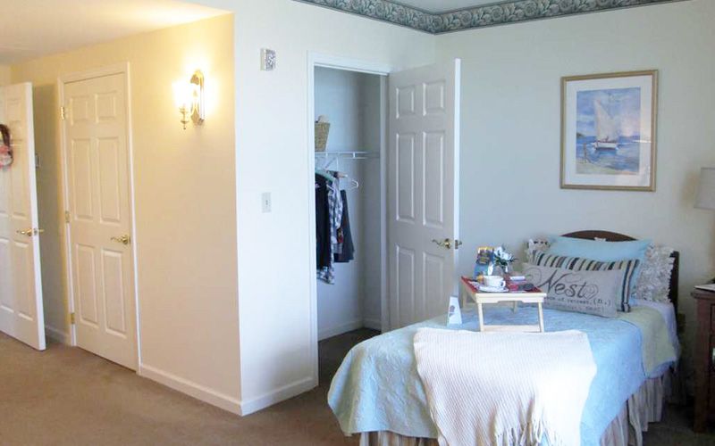 A cozy bedroom featuring a neatly made bed, a small tray on the bed, an open closet door, and soft natural lighting.
