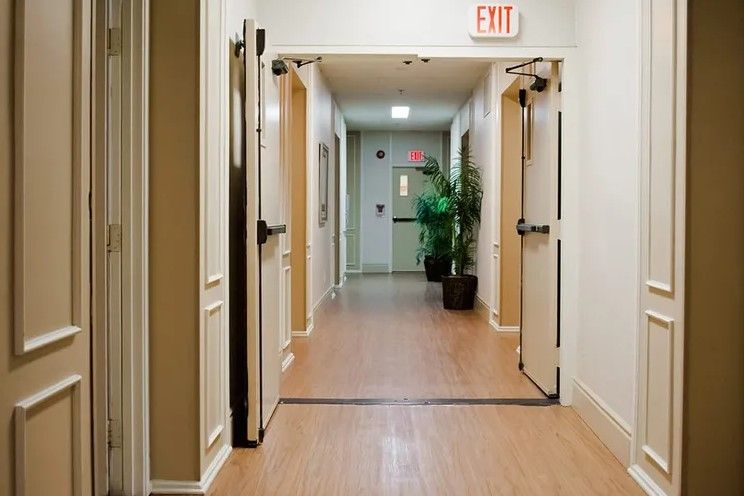 A well-lit hallway with open doors and an exit sign overhead.