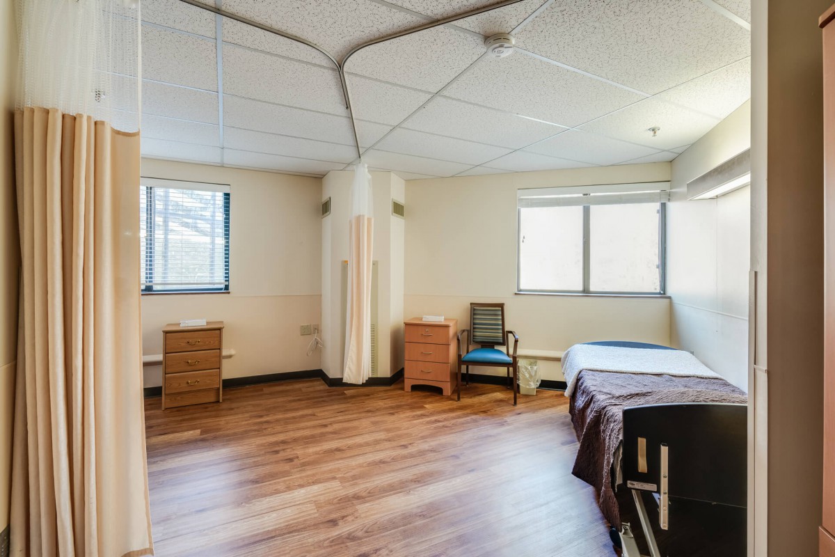 An empty room with a bed, desk, chair, and two windows.