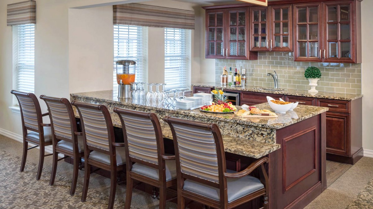 A modern kitchen with a granite countertop and chairs, featuring a fruit platter and glassware.