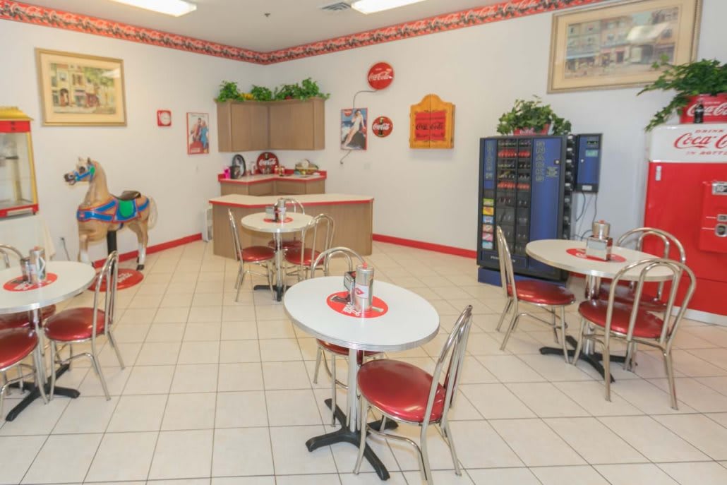 A retro-style diner with red and white decor, featuring tables, chairs, and a vending machine.