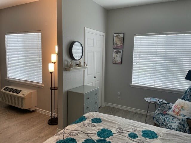 A modern bedroom with a bed, floor lamp, and two windows with blinds.