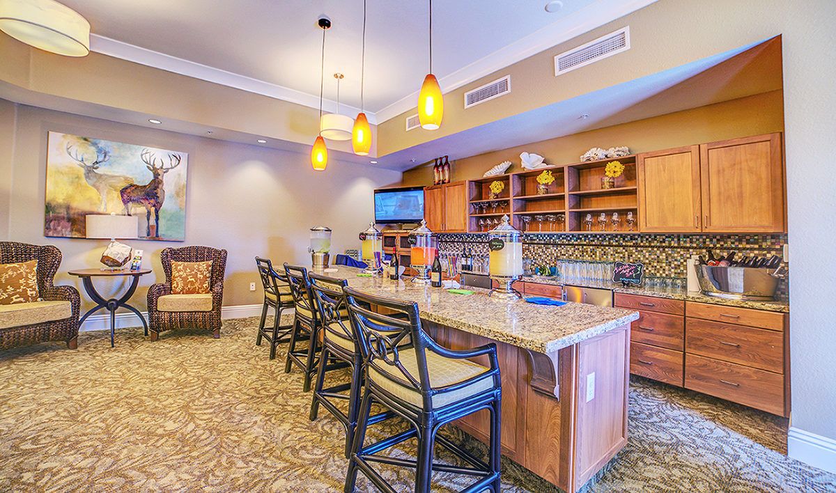 A cozy bar area featuring a spacious countertop with seating, ambient lighting, and decorative shelving.