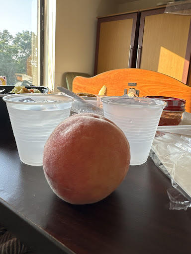 A peach in the foreground with two cups of water on a table.