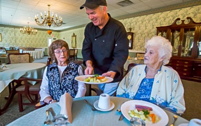 A chef serves a meal to two elderly women in a cozy dining setting.