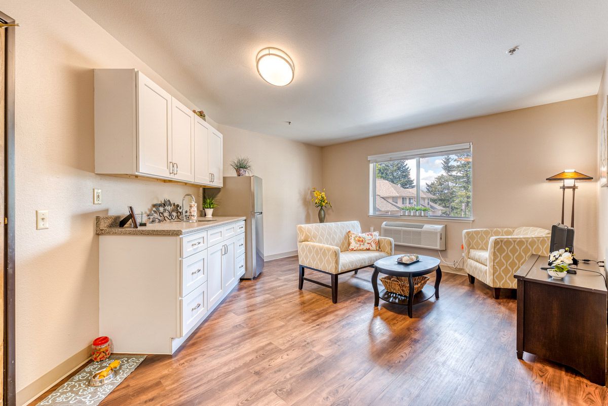 A cozy living area with an adjoining kitchen, featuring comfortable seating and large windows for natural light.