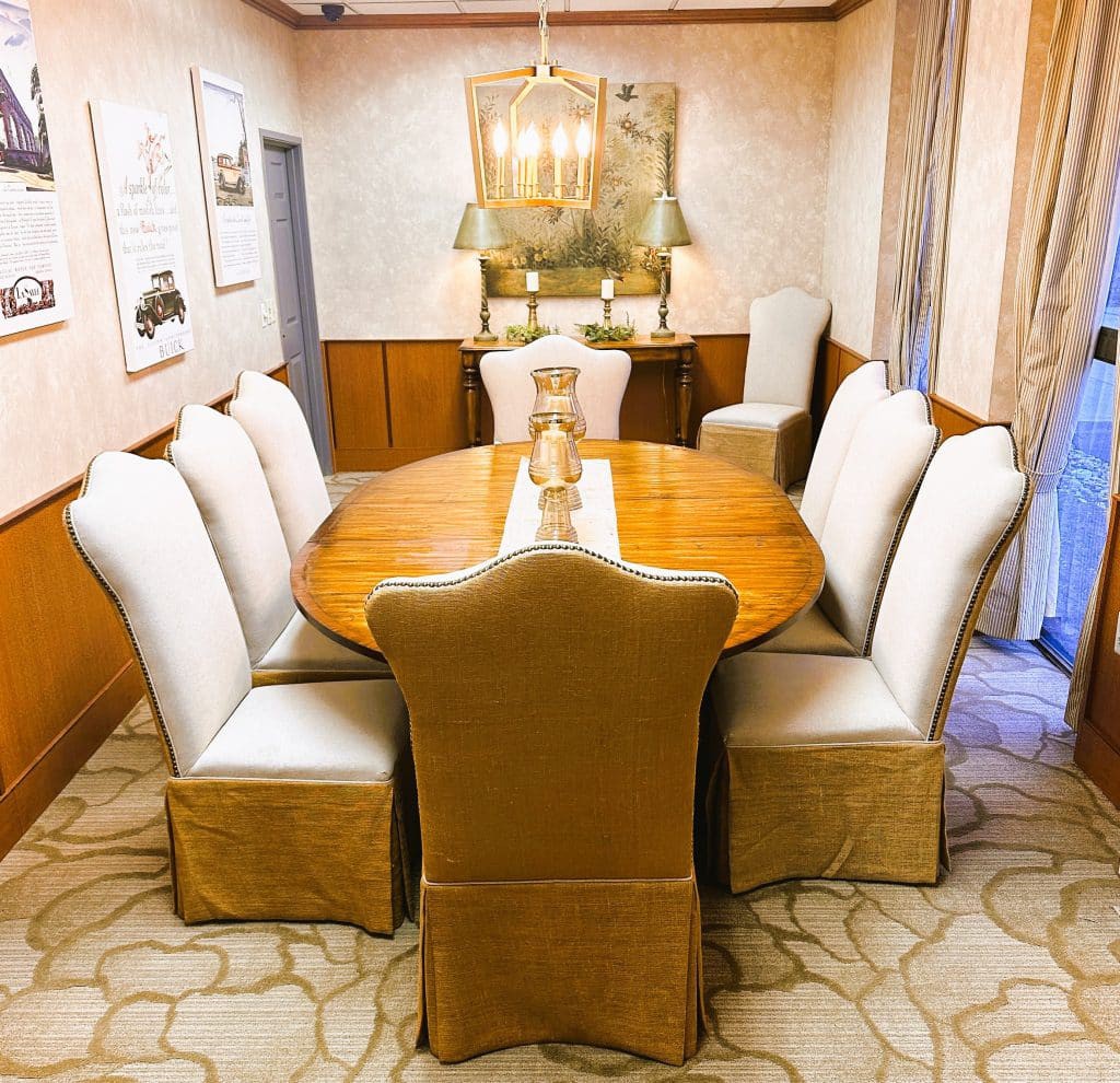 A well-decorated dining room featuring a large wooden table surrounded by upholstered chairs, with a chandelier overhead and framed artwork on the walls.