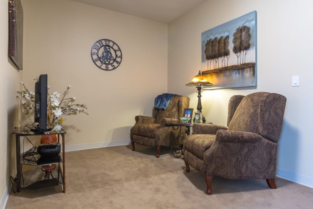 A cozy living room corner with two armchairs, a lamp, and decorative elements like a wall clock and painting.