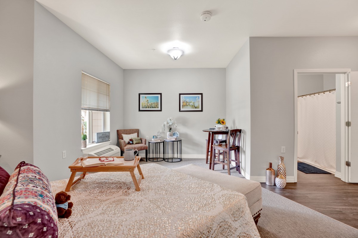 A cozy bedroom featuring a bed with a tray, an armchair, and wall art.