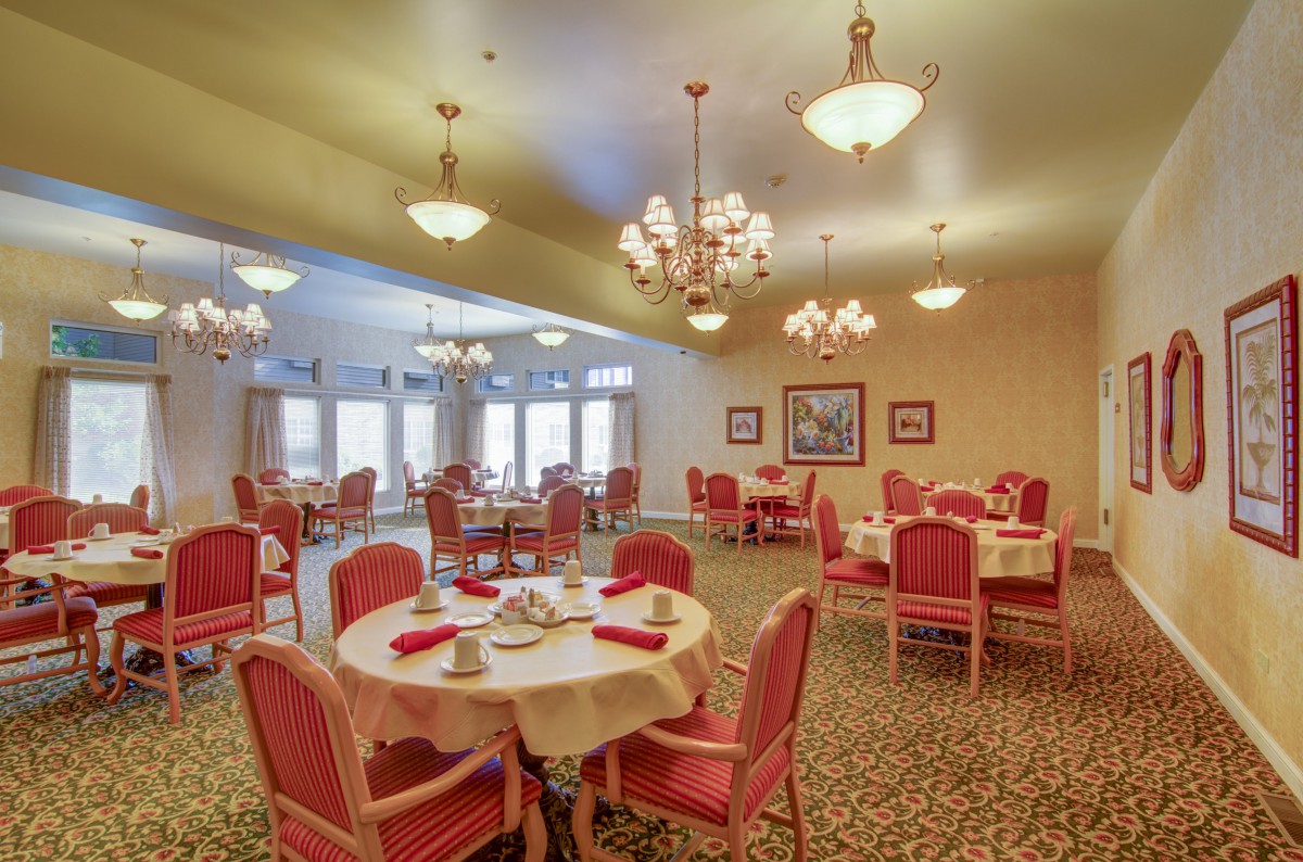 An elegant dining room with red chairs and chandeliers, featuring multiple round tables set for a meal.