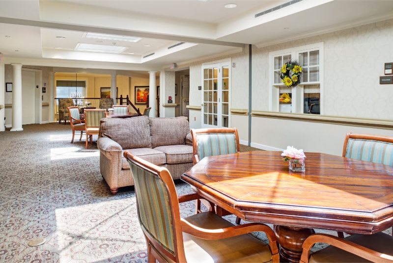 A cozy living room area with a wooden table, chairs, and a sofa under bright natural lighting.