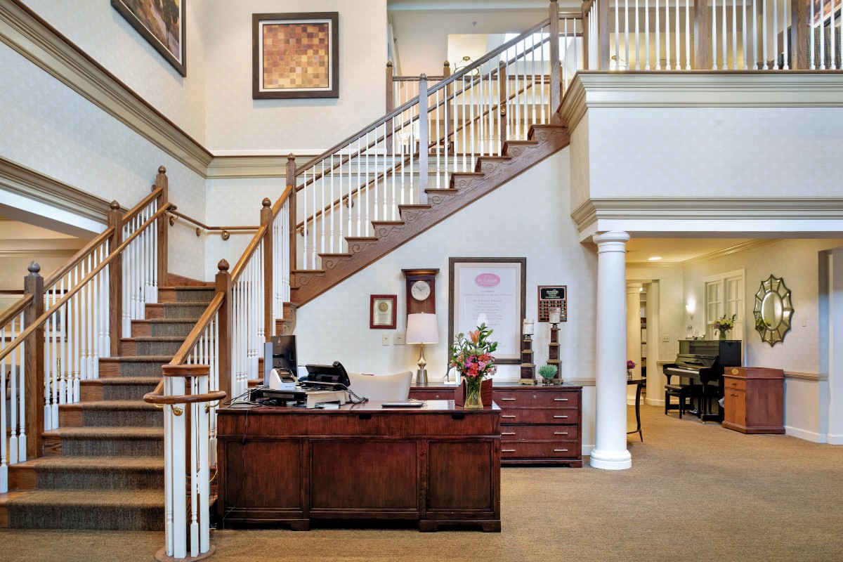 A reception area featuring a wooden desk, elegant staircase, and framed artwork.