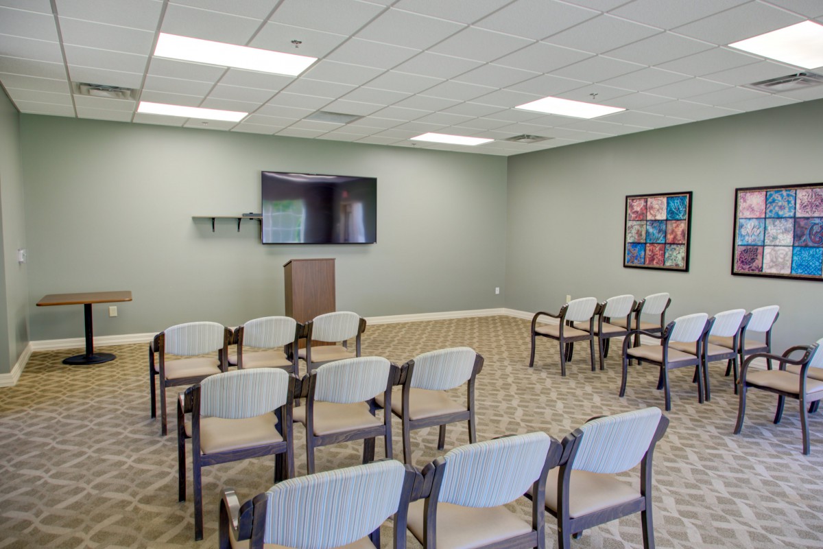 An empty conference room with arranged chairs, a podium, and a television screen.