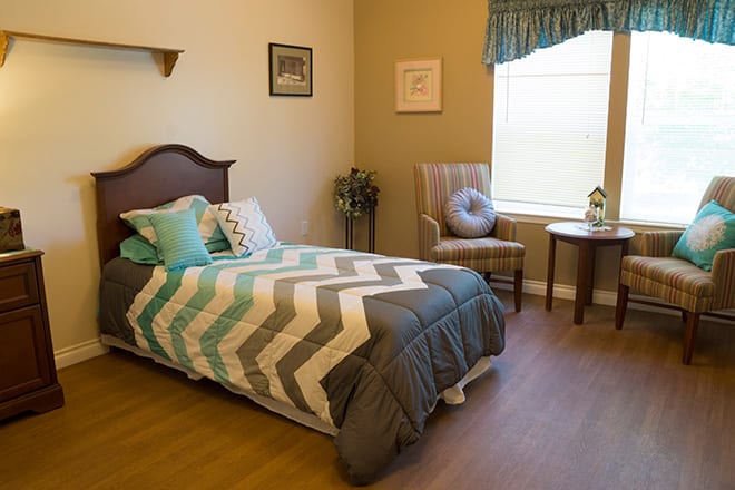 A cozy bedroom with a chevron-patterned bedspread, a chair by the window, and decorative elements.