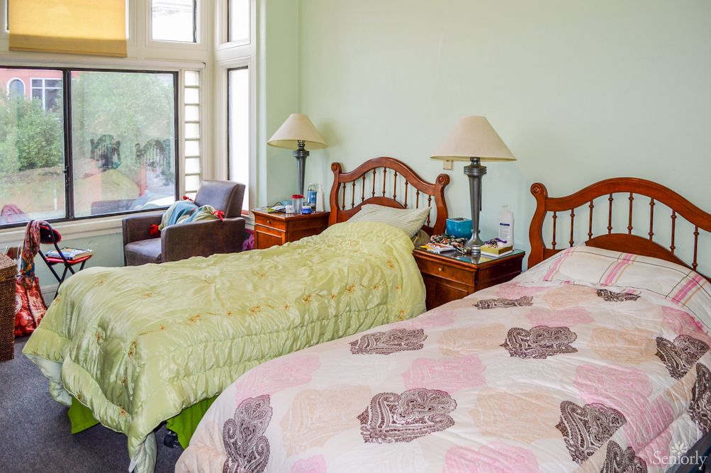 A cozy bedroom with twin beds, matching lamps on bedside tables, and a large window providing natural light.