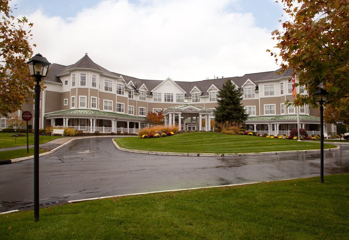 A large, elegant building with multiple gables and a landscaped driveway surrounded by autumn foliage.