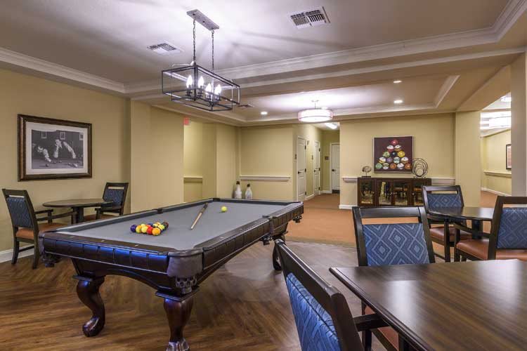 A recreational room featuring a pool table and comfortable seating, illuminated by elegant chandeliers.