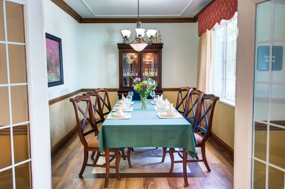 A neatly set dining room with a table and chairs, adorned with a floral centerpiece under a chandelier.