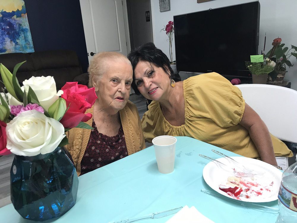 Two women sitting together at a table, smiling with flowers nearby.