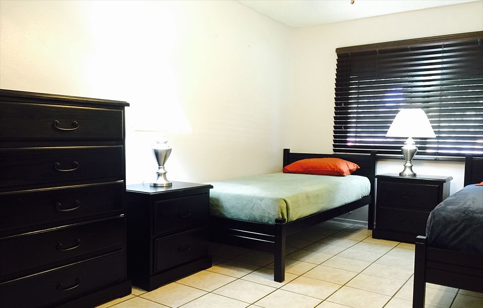A minimalist bedroom with a single bed, dresser, nightstand, and lamp.