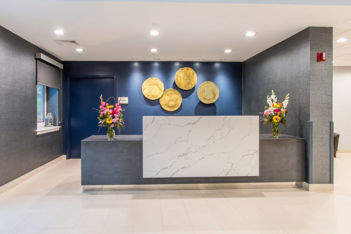A modern reception area featuring a marble desk, decorative wall art, and floral arrangements.