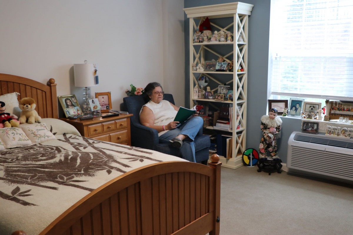 A person sits reading in a cozy bedroom with a bookshelf and decorations.