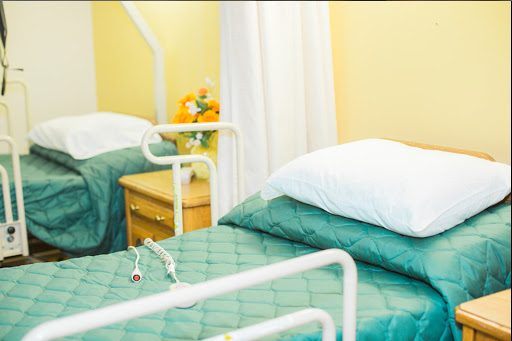 A serene hospital patient room featuring two beds with green bedding and a bedside table adorned with flowers.