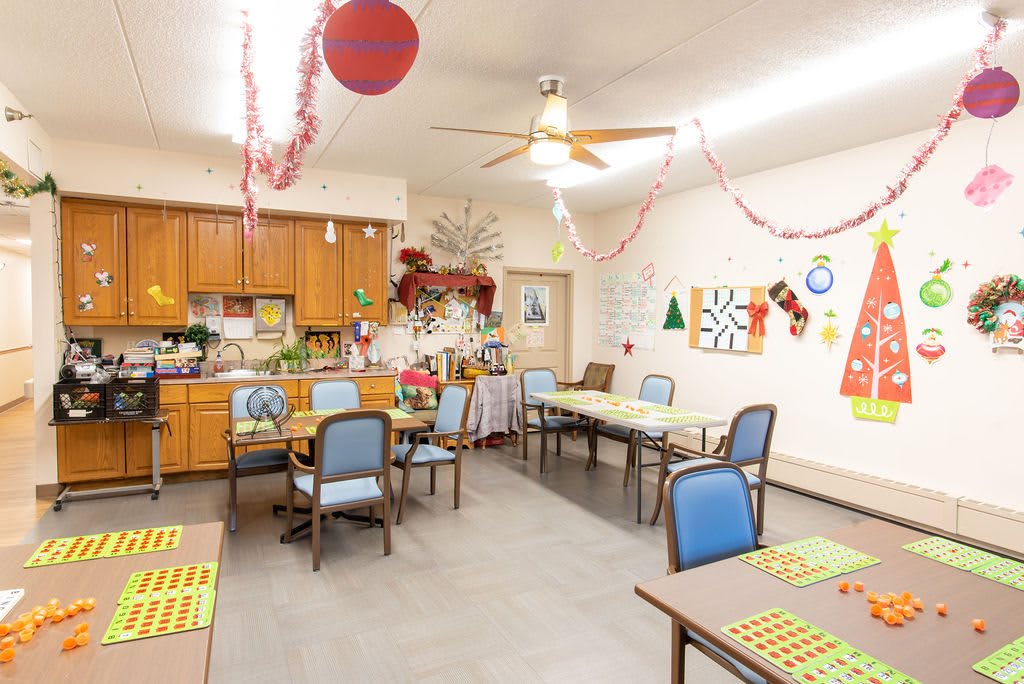 A decorated dining area with tables and chairs, featuring holiday decorations and a small kitchen space.