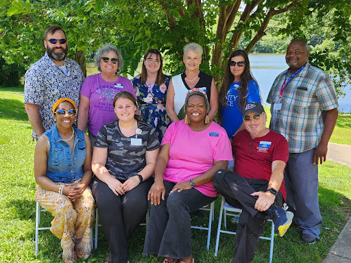 A group of individuals gathered outdoors, smiling together in a sunny setting.