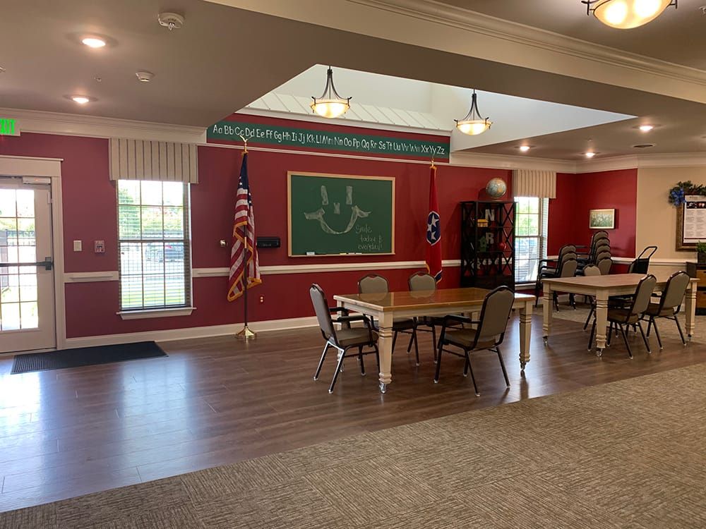 A spacious classroom with red walls, featuring tables, chairs, a chalkboard, and an American flag.