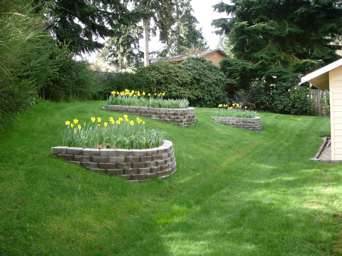 A landscaped garden featuring multiple retaining walls with flower beds on a grassy lawn.