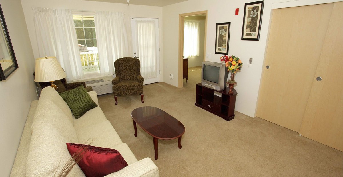 A cozy living room with a sofa, armchair, coffee table, and an old-style television.