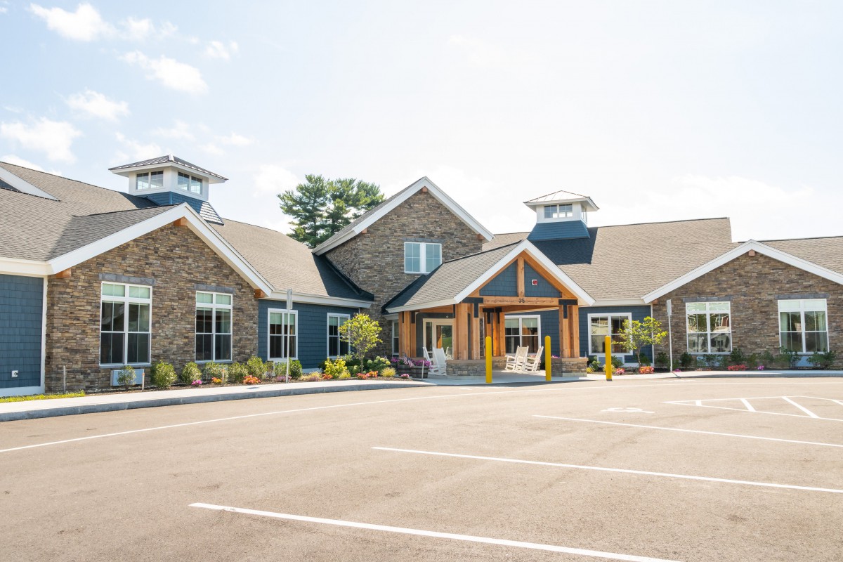 A modern commercial building with stone and wood accents, situated in a parking lot under a clear sky.