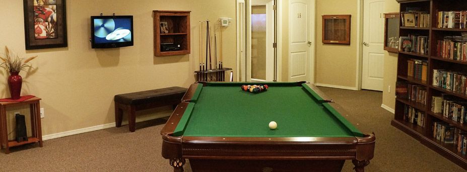 A billiards room featuring a green pool table with cue sticks in the background.