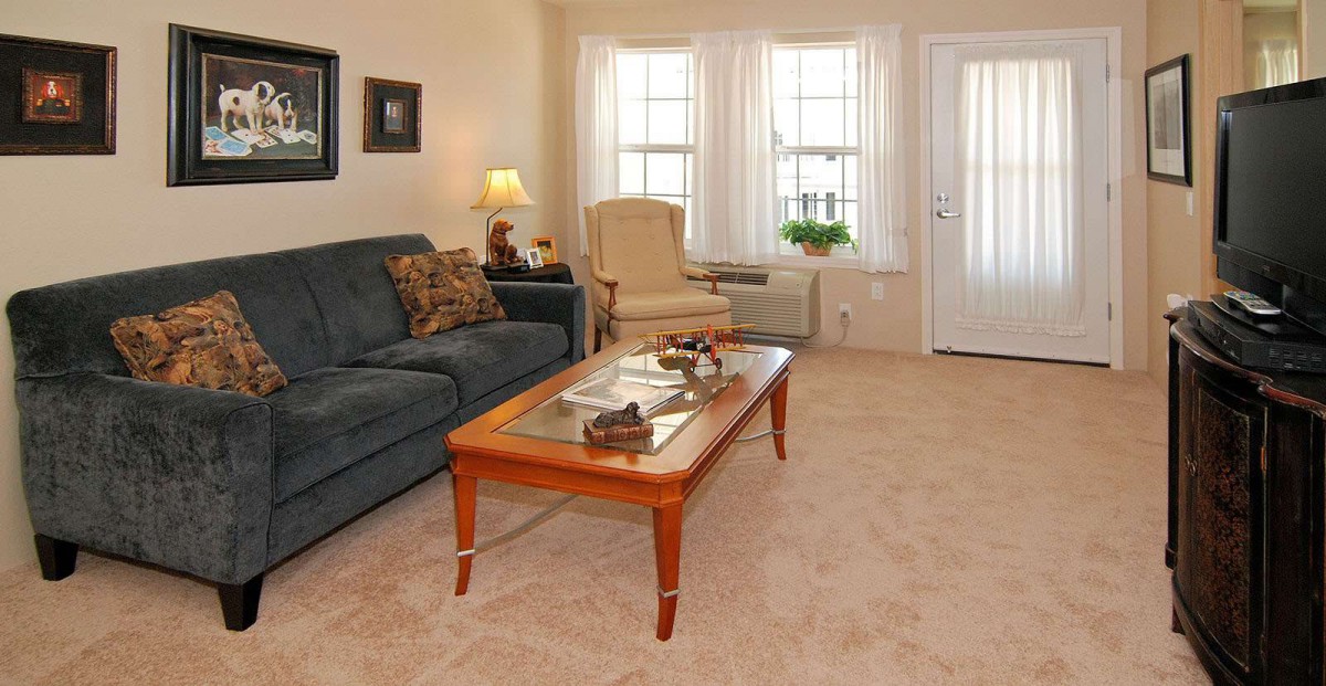 A cozy living room with a sofa, coffee table, armchair, and large windows.