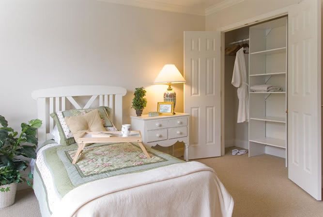 A cozy bedroom with a neatly made bed, a nightstand with a lamp, and an open closet.