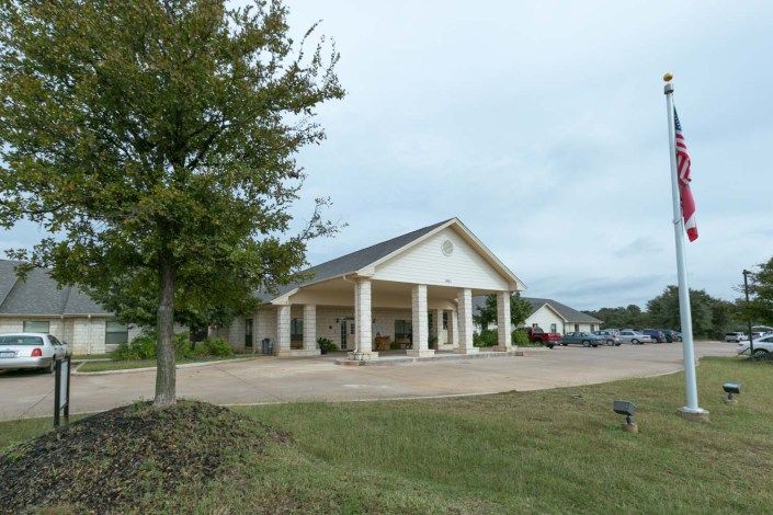A single-story building with columns, surrounded by a grassy area and parking lot.