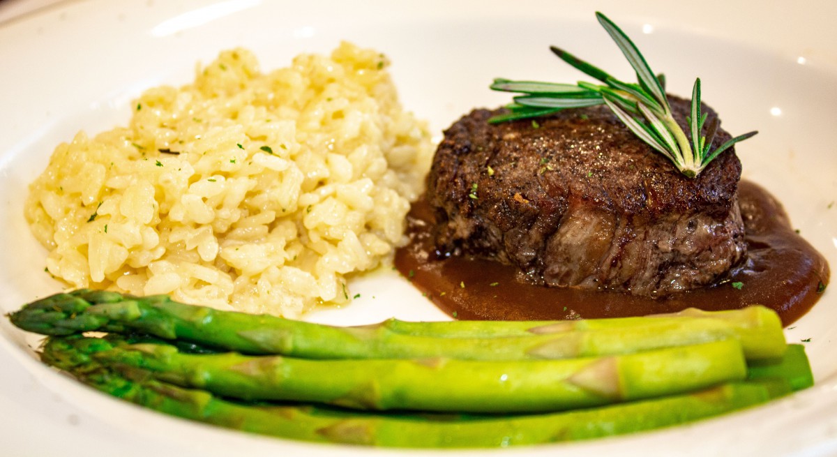 A gourmet dinner plate featuring steak with rosemary, risotto, and asparagus.